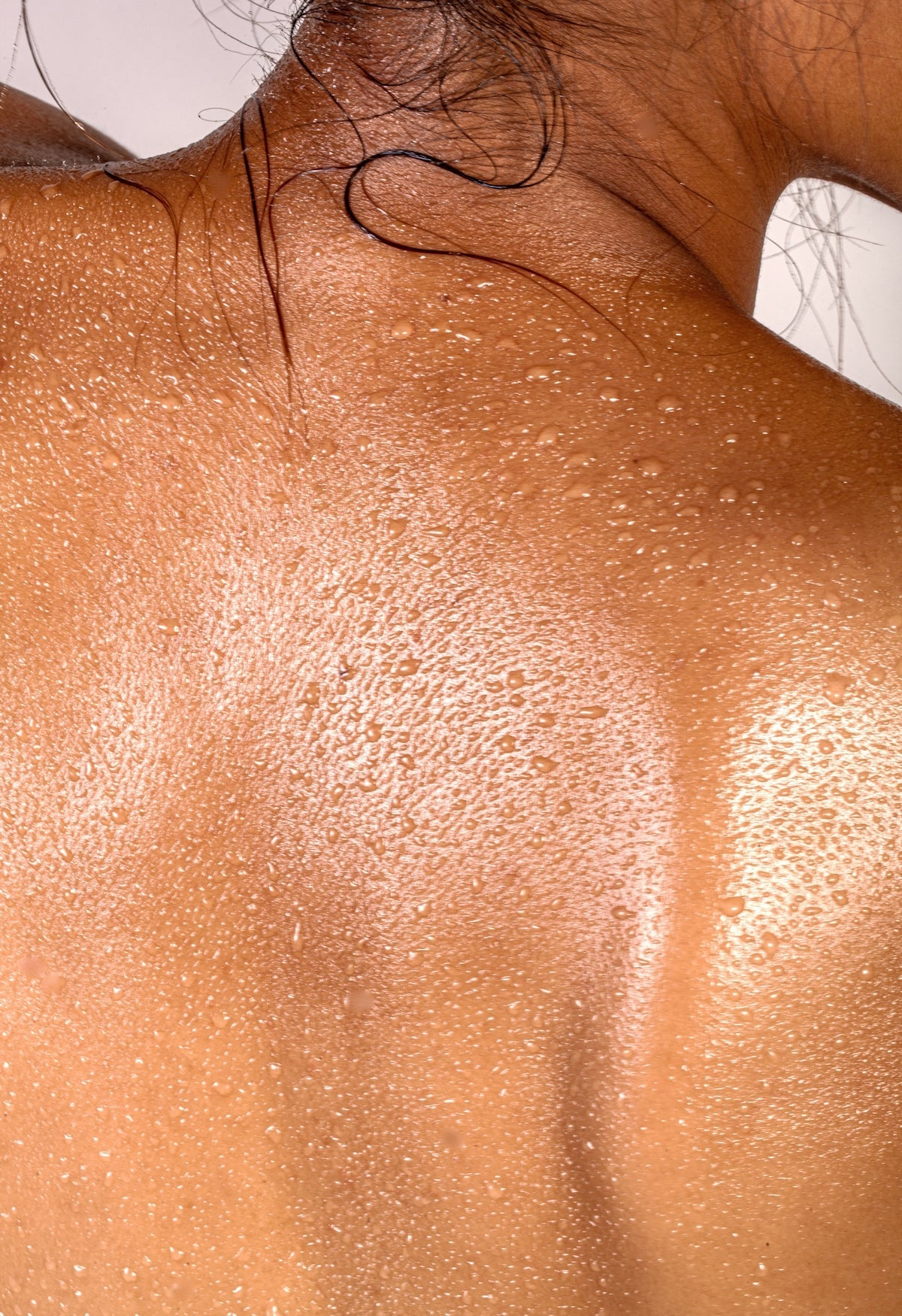 A person's back covered in small beads of sweat with dark hair strands